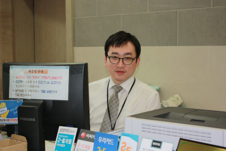 2003년 병원 원무과 창구에서 근무하는 글쓴이. 모니터 옆에 제증명 발급 안내문이 붙어 있다.